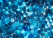 Close-up of densely packed blue glass spheres occupying the frame, varying in size and translucence.