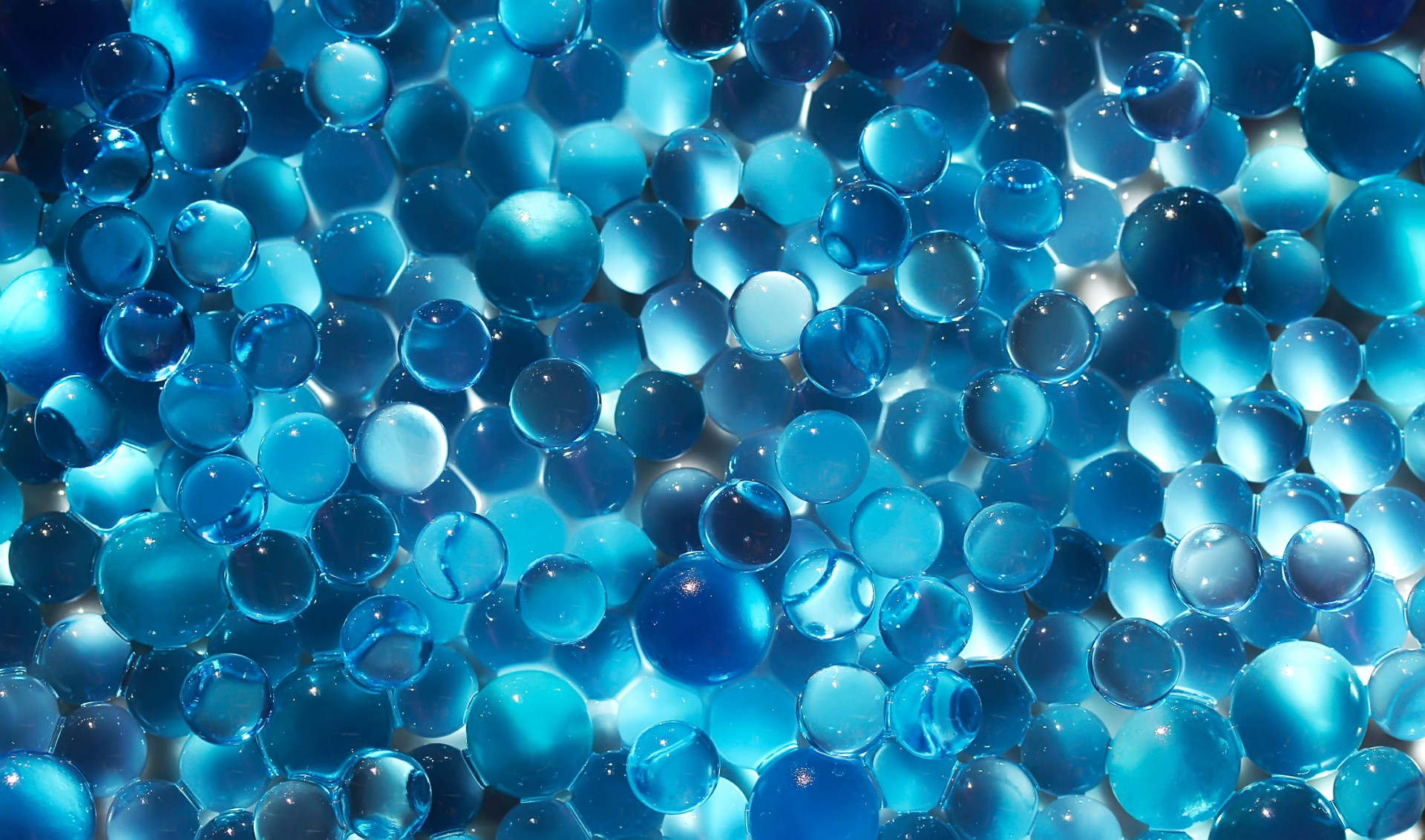 Close-up of densely packed blue glass spheres occupying the frame, varying in size and translucence.